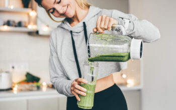 Young Woman Making Detox Smoothie At Home. Woman pouring smoothie to glass. healthy food concept