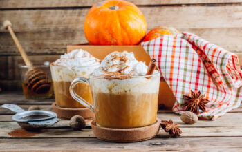 Pumpkin spiced latte in a glass mug on a vintage wooden background. Autumn or winter hot drink. Selective focus