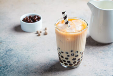 Milk bubble tea with tapioca pearls in a glass, gray background.