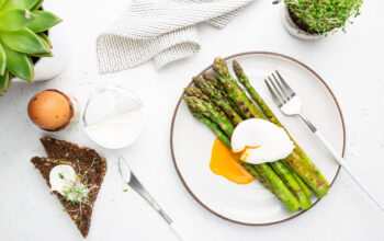 Roasted asparagus with poached egg on plate on white background, top view