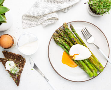 Roasted asparagus with poached egg on plate on white background, top view